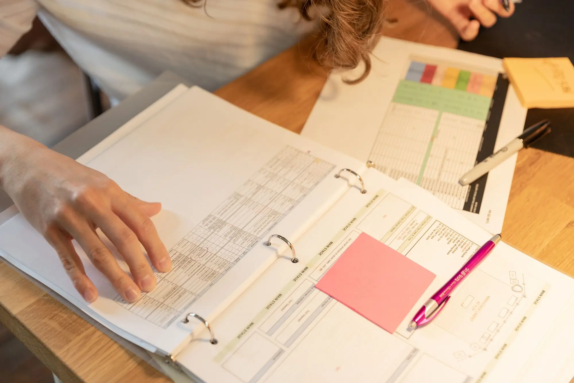 Business owner working through a ring binder of financial records with sticky notes and pens on a wooden desk